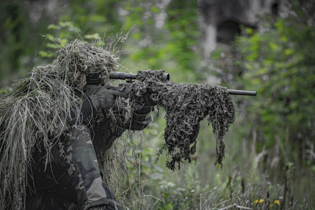 Joueur d'airsoft en tenue ghillie visant avec une réplique de sniper